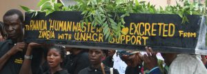 Réfugiés portant un tombeau sur lequel est inscrit " Excréments humains à expédier au Rwanda en provenance de Zambie avec le support du HCR" Réfugiés portant un tombeau sur lequel est inscrit " Excréments humains à expédier au Rwanda en provenance de Zambie avec le support du HCR"